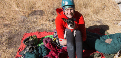 A small dog sits in a woman's lap while they are out in nature. 