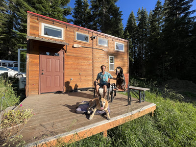 A man and his two dogs sit on the front porch of their tiny house. 